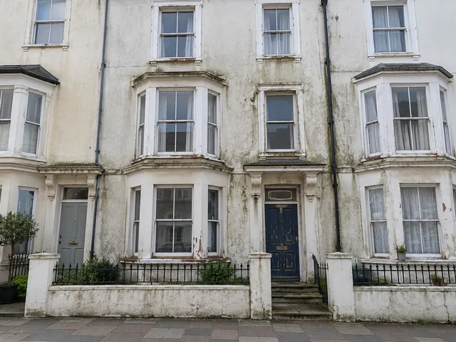 A rendered seafront terrace with grubby, weather-stained walls and flaking window paint.