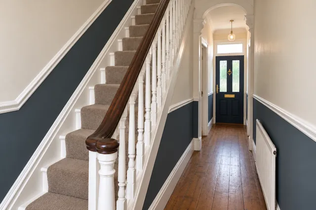 The same hallway with off-white walls, a navy lower half, white spindles and a navy front door.